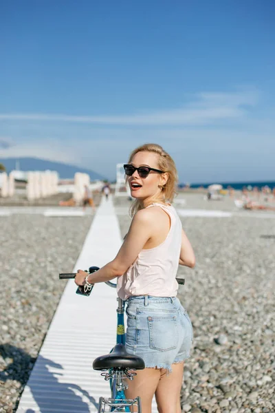 Kvinnan lutar sig på cykeln, stående nära observationsdäck på stranden — Stockfoto