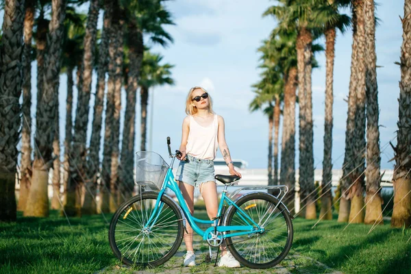 Γυναίκα στέκεται κοντά νοικιασμένο ποδήλατο στο πάρκο. Καλοκαίρι και τρόπος ζωής — Φωτογραφία Αρχείου