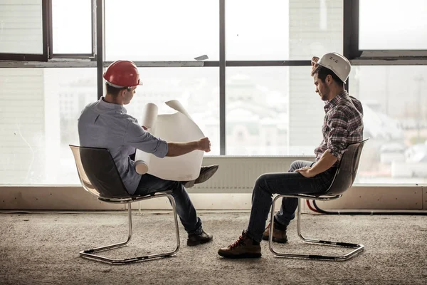 Engenheiro está abrindo o plano enquanto seu parceiro está colocando um chapéu duro — Fotografia de Stock