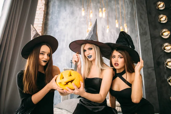 crazy glamour party, three mistress in elegant wear, with bright red lips, long wizard headwears, standing posing on white wall background, with pumpkin cutted head, enjoying, like stars