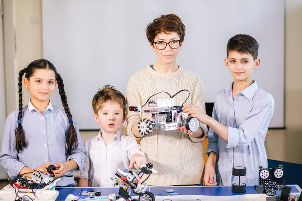 education, science, technology, children and people concept , Pleasant young engineer mother showing her children using laptop how to construct and programme plain robot kits