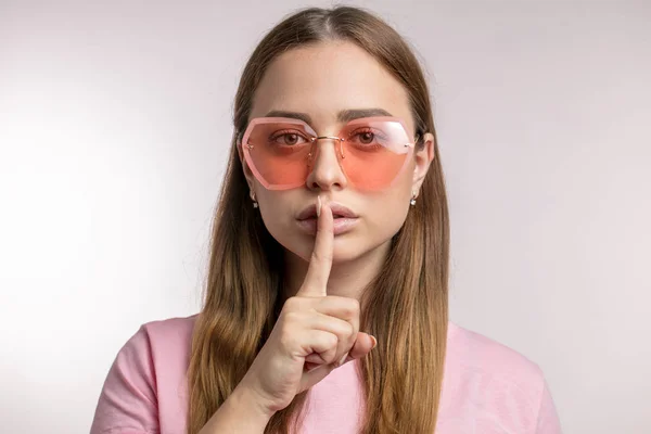 Ernste junge stylische Frau mit pinkfarbener Sonnenbrille macht eine ruhige Geste — Stockfoto