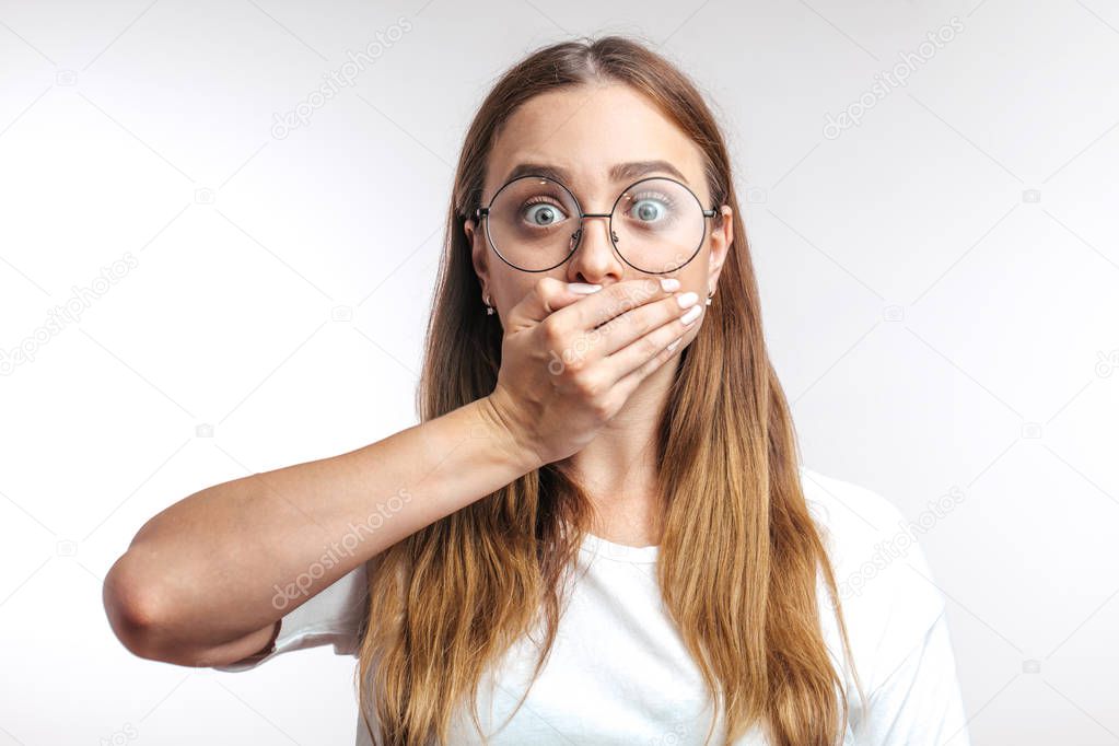 Young surprised Caucasian woman closing her mouth with hand on white background