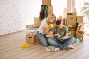 couple with book sitting on bed while moving into new home clipart