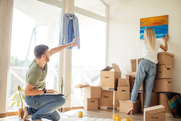 Casa de mudanza. Pareja colgando imagen en la pared en un nuevo hogar — Foto de Stock