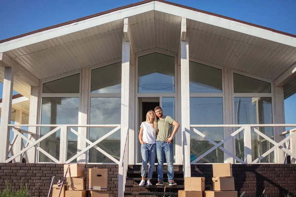 Marido e esposa em pé na frente de nova compra de casa com caixas — Fotografia de Stock