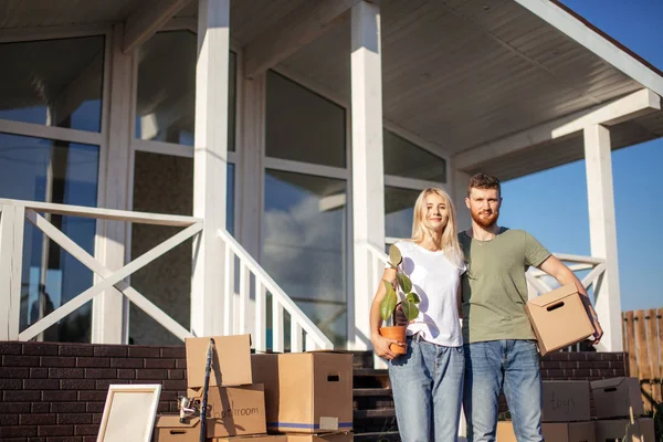 Муж и жена стоят перед новой покупкой дома с коробками — стоковое фото
