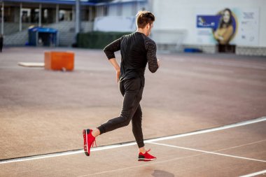 Siyah spor giyimli erkek sporcu hipodromda koşuyor.