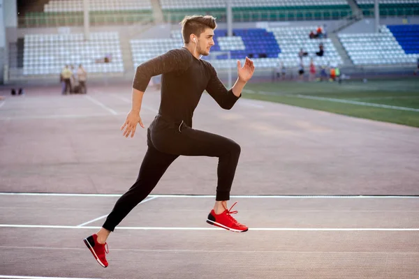 Male athlete wearing black sportwear running at track, side view — Stock Photo, Image