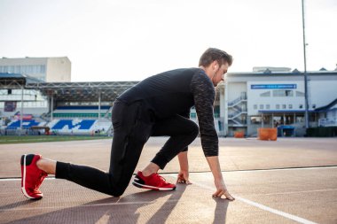Sporcu koşu pistinde başlangıç pozisyonunda. Stadyum pistinde koşu antrenmanı yapan koşucu