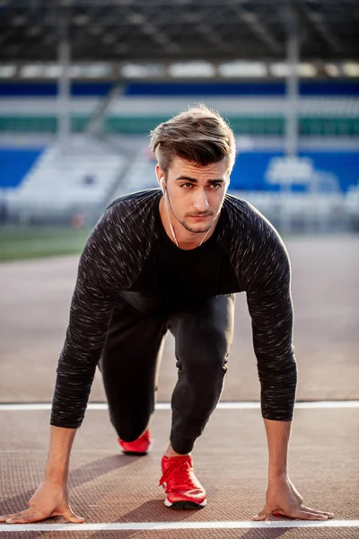 Atleta en posición inicial en pista de atletismo. Corredor practicando carrera en pista de carreras de estadio —  Fotos de Stock