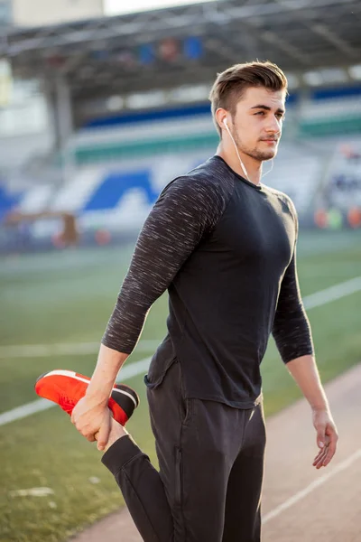 Hombre estira el cuerpo antes de correr en pista de carreras en el estadio —  Fotos de Stock