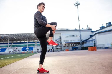 Adam stadyumdaki yarış pistinde koşmadan önce vücudu gerer.