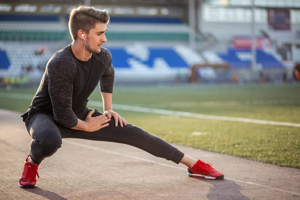 Man stretches the body before running on race track in stadium — Stock Photo, Image
