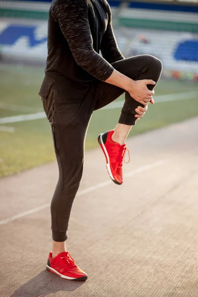 Man stretches the body before running on race track in stadium — Stock Photo, Image