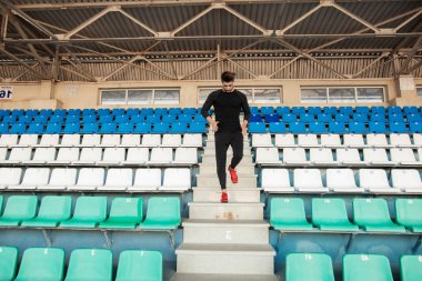 Siyah elbiseli, formalı bir adam spor stadyumunda koşuyor.