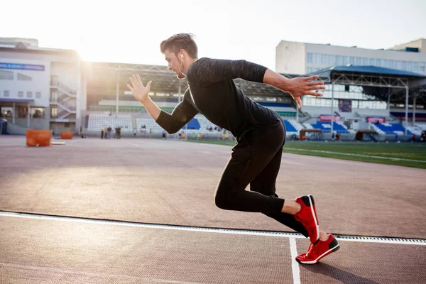 Athlete in black clothes starting sprint on running track — Stock Photo, Image