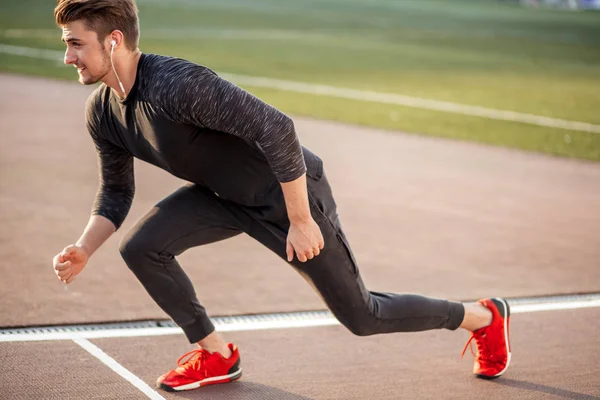 Atleta en ropa negra comenzando sprint en pista de running —  Fotos de Stock