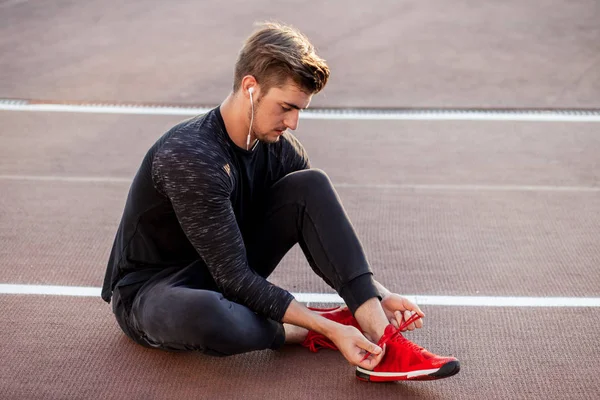 Runner preparándose para correr atando cordones de zapatillas mientras está sentado en la pista —  Fotos de Stock