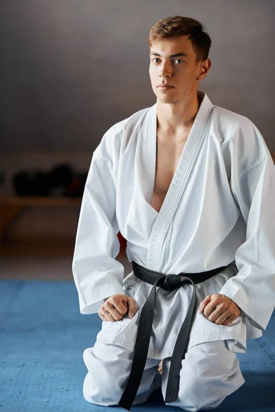 Karate man in kimono zit op knieën op de vloer in de sportzaal martial arts — Stockfoto