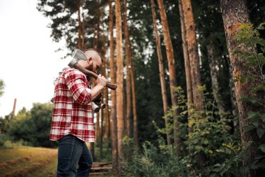 Omuzlarında balta ve yakacak odunları olan sakallı adam.
