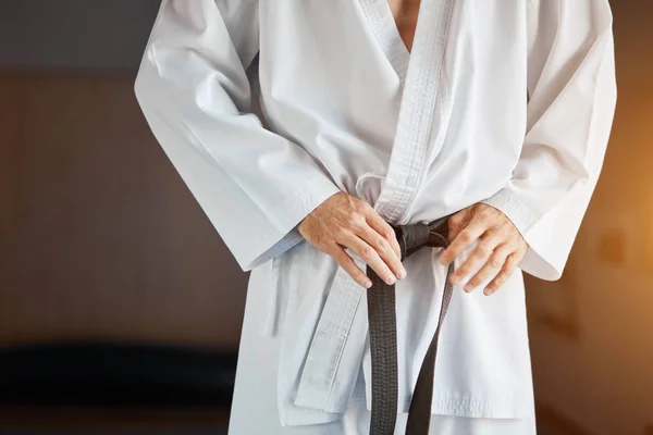 Hands tightening black belt on man dressed in kimono