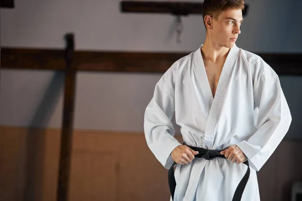 Руки затягивают черный пояс на человеке, одетом в кимоно — стоковое фото