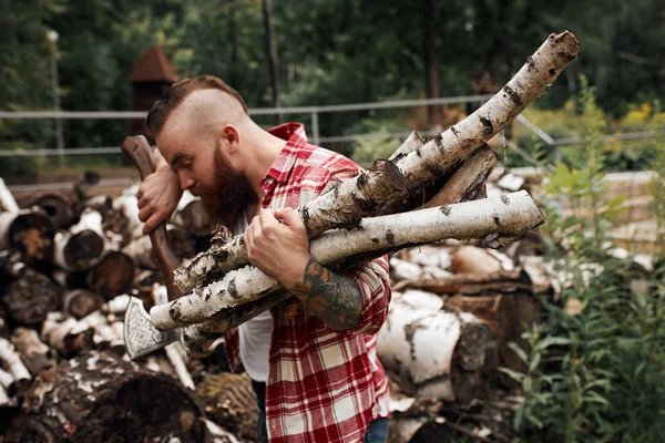 Bearded Man with firewoods and with axe on shoulder — Stock Photo, Image