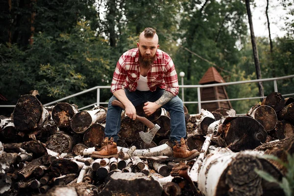 Mannen sitter i en eldstad. Träskärare med yxa vilar efter arbete — Stockfoto