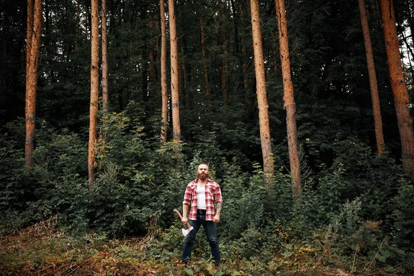 Bearded Lumberjack worker standing in forest with axe — Stock Photo, Image