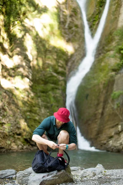 Молодой турист кемпинг с рюкзаком возле водопада в лесу. — стоковое фото