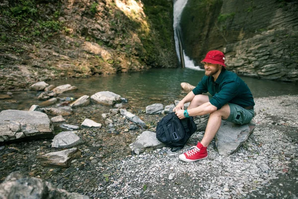 Mladý turistický kemp s batohem v blízkosti vodopádu v lese. — Stock fotografie