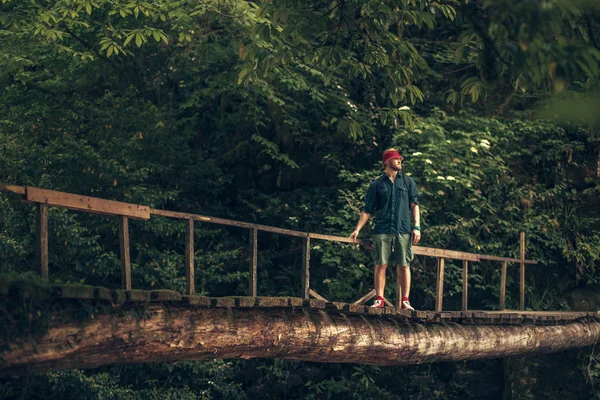 Cestovatel prochází visutým mostem v zeleném letním lese. — Stock fotografie