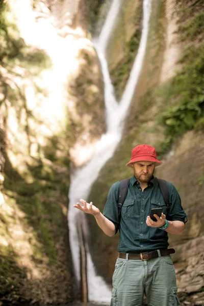 Randonneur tient smartphone essayant de trouver une connexion dans la forêt profonde avec cascades. — Photo