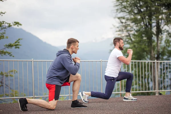 Sidovy av två kaukasiska idrottsmän gör lungesin berg. — Stockfoto