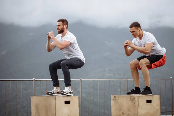 Kaukasiska manlig atletisk vänner gör rutan hoppa utomhus på toppen av berget. — Stockfoto