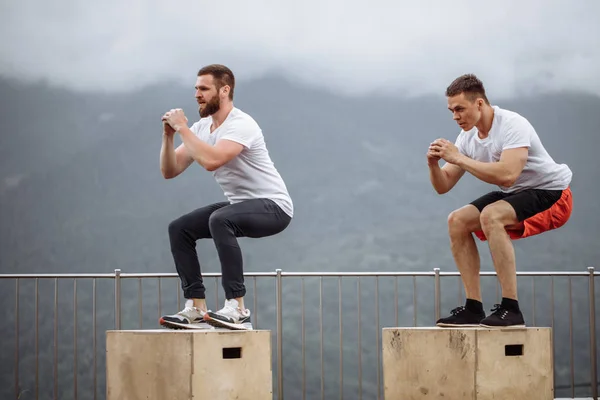 Caucásico macho atlético amigos haciendo caja salto al aire libre en la cima de la montaña . — Foto de Stock