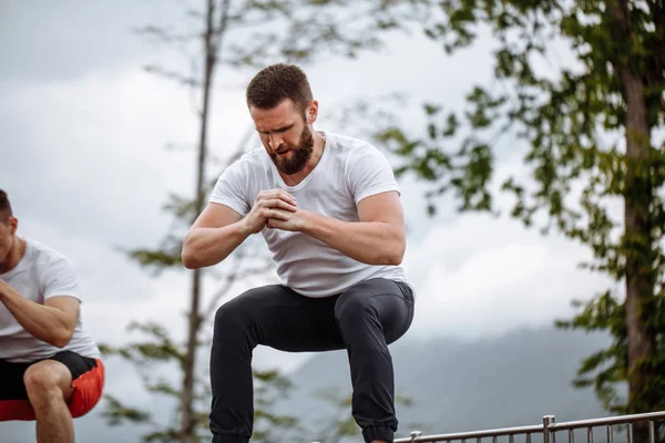 Dos amigos atléticos masculinos haciendo salto de caja al aire libre en la cima de la montaña. — Foto de Stock