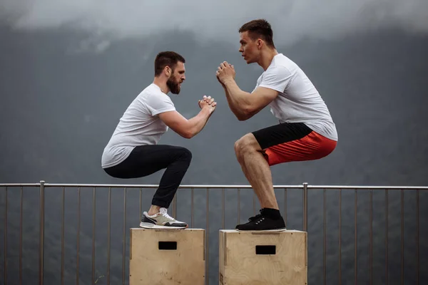 Dos amigos atléticos masculinos haciendo ejercicio de salto de caja al aire libre — Foto de Stock