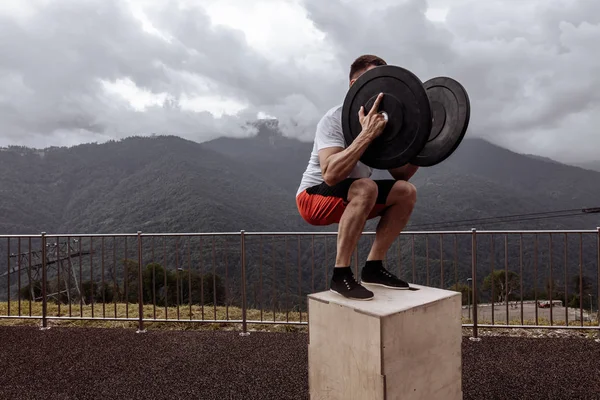 Stark manlig idrottsman gör box hopp med två plattor utomhus på toppen av berget. — Stockfoto