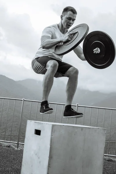 Strong male athlete doing box jumps with two plates outdoor on top of mountain. — Stock Photo, Image