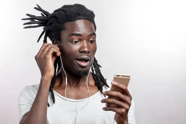 Homem africano usando fones de ouvido e segurando seu smartphone contra fundo branco — Fotografia de Stock