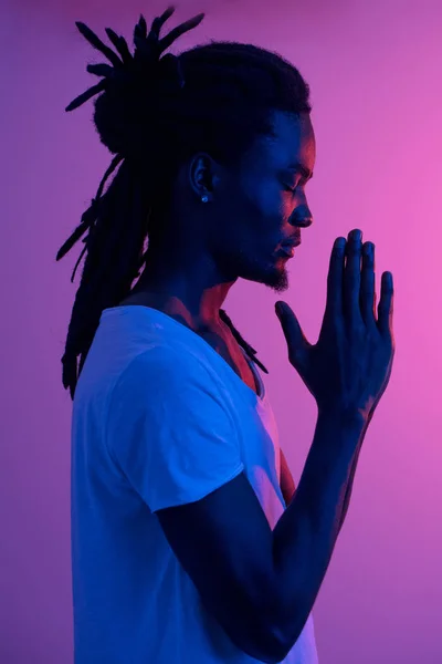 Close up of black man with dreadlocks praying on purple background — Stock Photo, Image