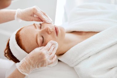 Kozmetik uzmanı pamuklu ped takıyor. Kadın yüzü ameliyata hazırlanıyor..