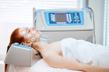 Yüzünde elektrotlar olan genç bir kadın, elektrik uyarısı alıyor..