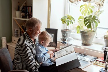Büyükbaba ve torun evdeki kanepede. Büyükbaba ve çocuklar eski fotoğrafları izliyor.