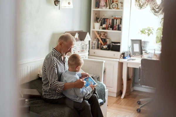 Abuelo y nieto usando tableta digital mientras están sentados en el sofá — Foto de Stock