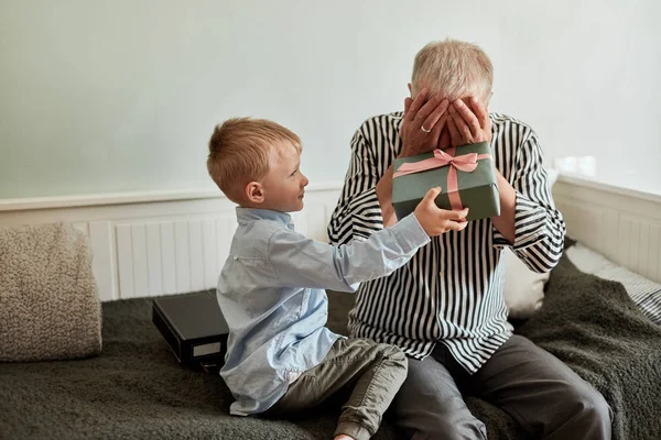 Generation. farfar och sonson med presentförpackning sittandes på soffan hemma — Stockfoto