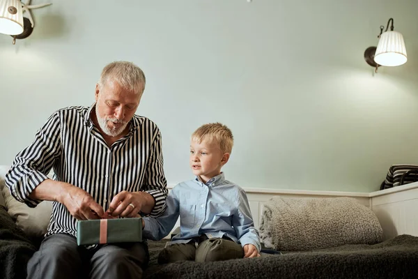 Покоління. дід і онук з подарунковою коробкою, що сидить на дивані вдома — стокове фото