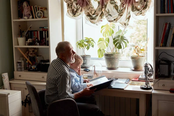 Abuelo y nieto en el sofá en casa. Abuelo y niños viendo fotos viejas — Foto de Stock